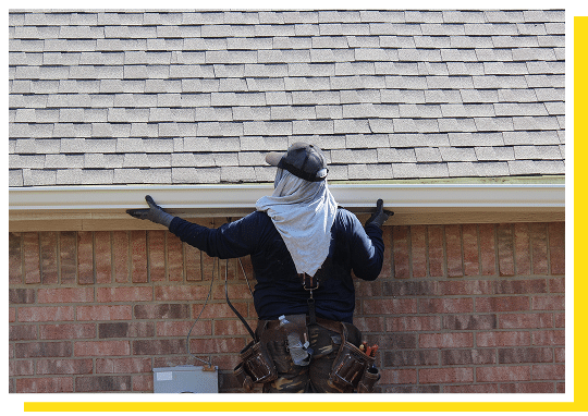 Homeowner clearing leaves and debris from a gutter along the roof edge during spring maintenance