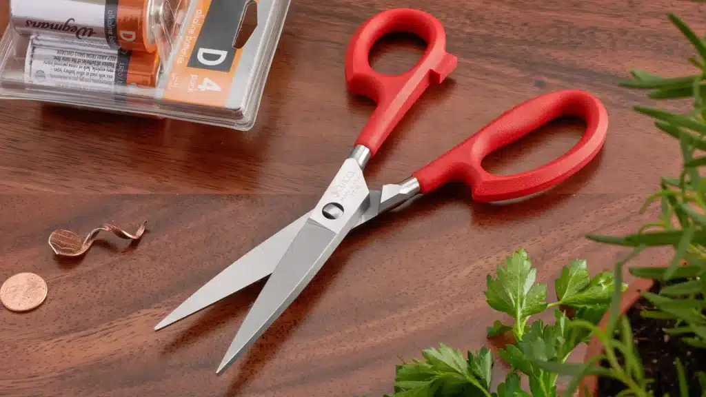 kitchen scissors with red handles beside fresh herbs on a countertop