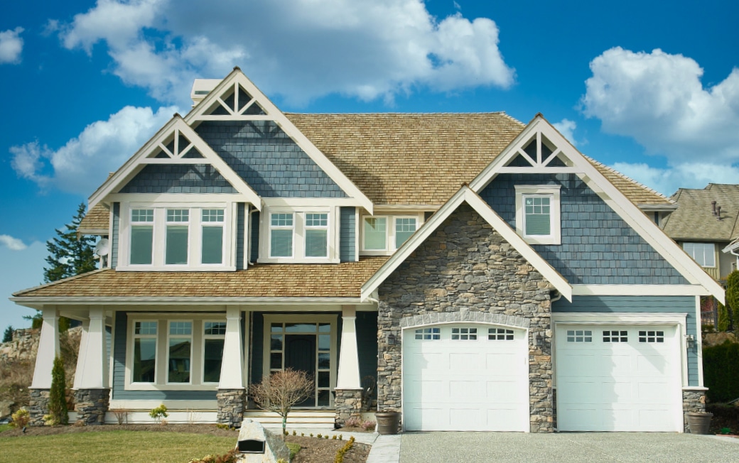 Two-story residential home with shingle roof, stone exterior, and attached garage